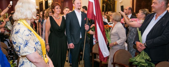 Skolas vadība un izcilnieki zālē ienes Latvijas un skolas karogus.